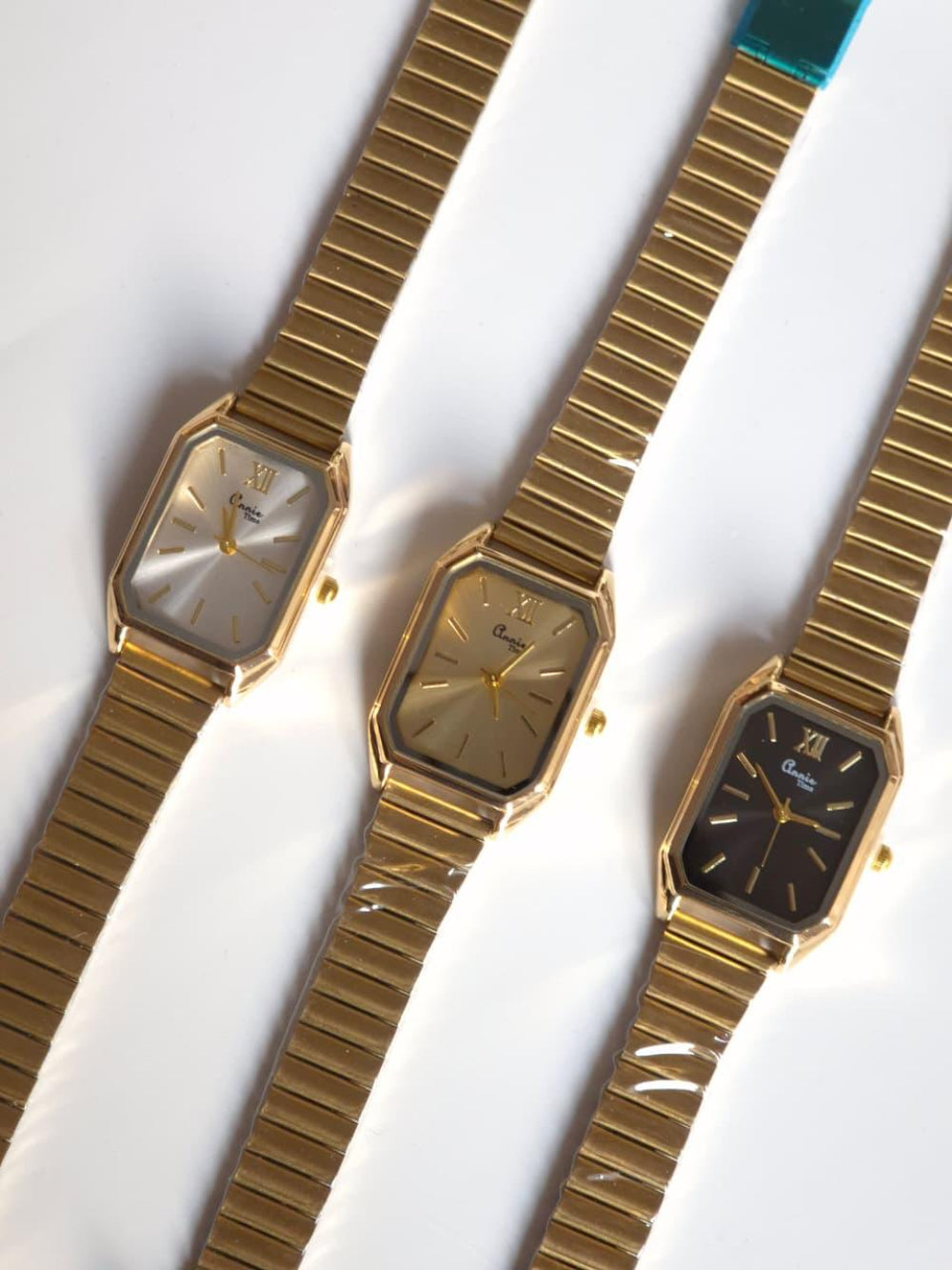 Three gold wristwatches with different face colors on a white background