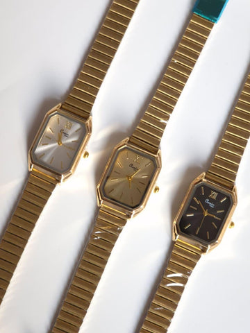 Three gold wristwatches with different face colors on a white background