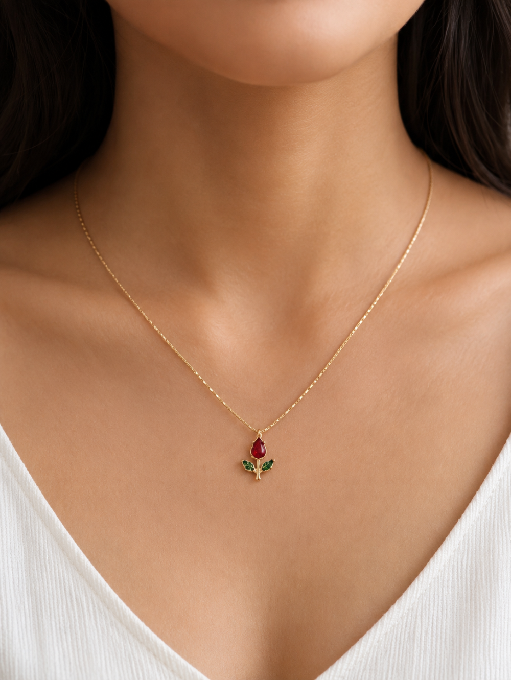 Gold necklace with a pendant featuring a red gemstone and green leaves