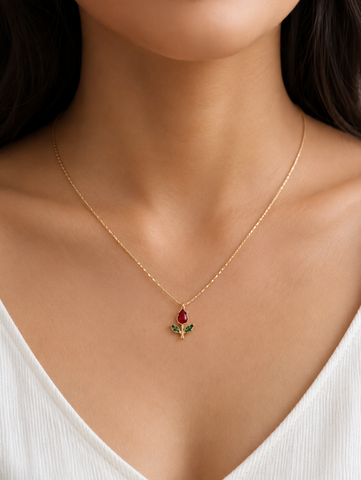 Gold necklace with a pendant featuring a red gemstone and green leaves